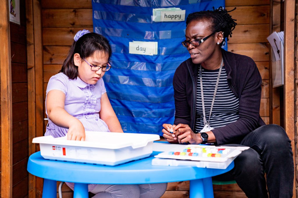 A teaching assistant supporting a blind child with their work using braille.